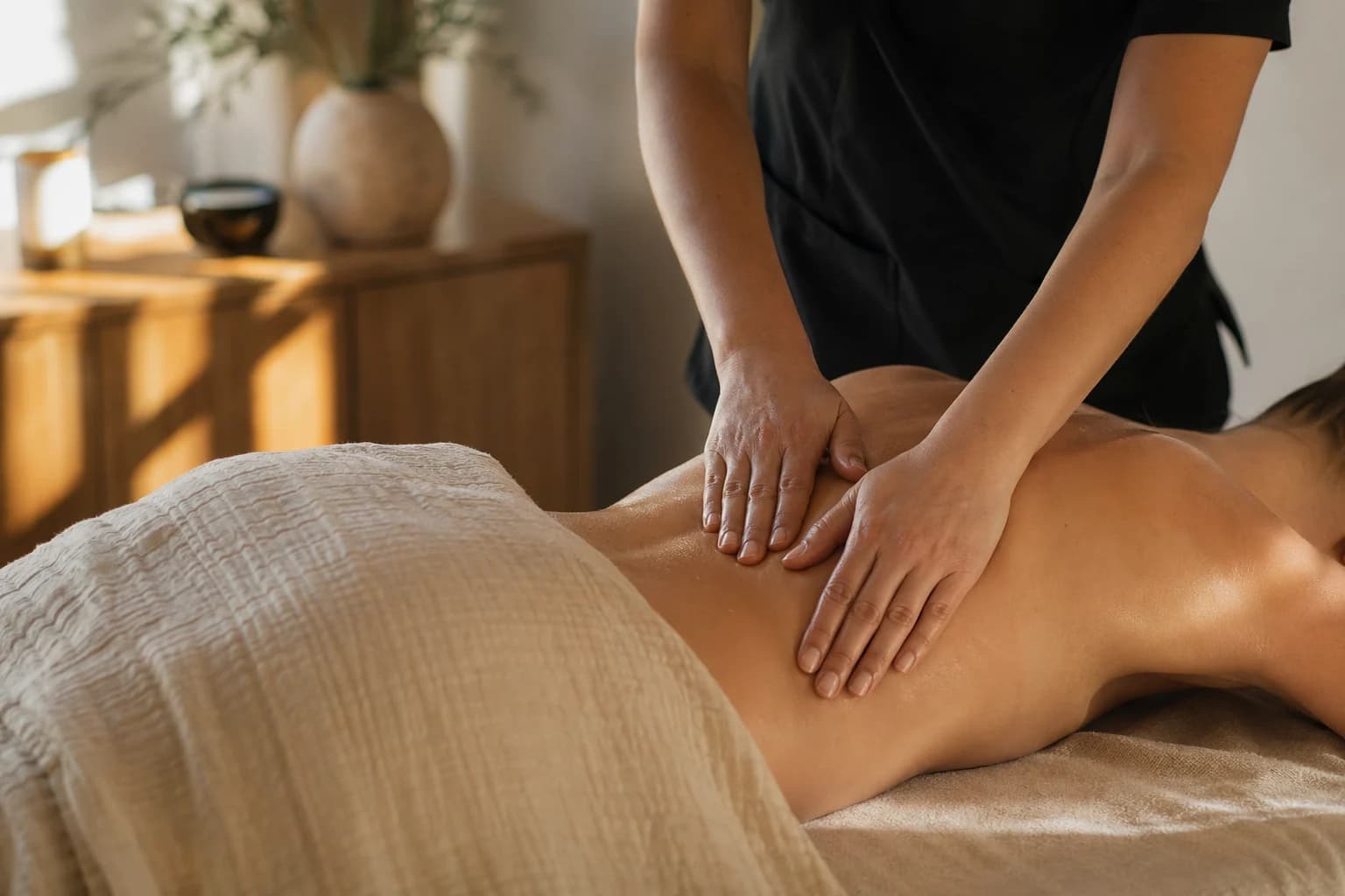 Therapeutic massage in a calm treatment room with warm linen and soft daylight.